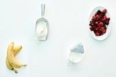 Flour, berries, bananas and cream on white background