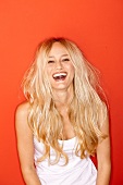 Portrait of happy woman with long hair wearing white top laughing against red background