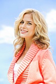 Portrait of beautiful young woman with blonde hair wearing peach sweater, smiling