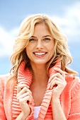 Portrait of beautiful blonde woman wearing peach sweater smiling and turning her collar 