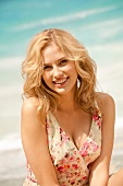 junge Frau im Sommerkleid am Strand, lächelt in die Kamera