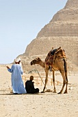 Arab people sitting with camel in desert against Pyramid of Djoser, Saqqara, Egypt