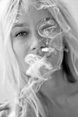 blonde Frau mit Zigarretten qualm vor dem Gesicht