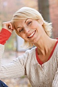 Pretty blonde woman with short hair wearing white sweater resting head on hand, smiling