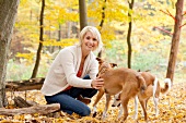 Blonde Frau in beigefarbenener Jacke spielt mit zwei Hunden