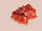 Raw thinly sliced serrano ham on beige background