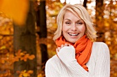 Pretty blonde woman with short hair wearing white sweater, smiling in autumn forest