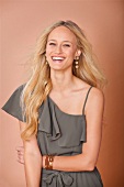 Portrait of happy blonde woman with long hair in gray dress and long earrings, laughing