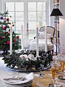 An advent wreath with silver Christmas decorations and white candles on a table