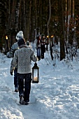 Kids wearing winter clothes holding lamp and torches walking in snow