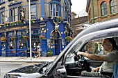 Black taxi passing across The Shipwrights Arms pub, Southwark, London, UK