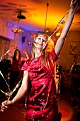 Happy woman wearing red satin dress celebrating while dancing at New Year's Eve party