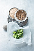 Broccoli in baking paper besides bamboo baskets on white background