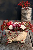 Hagebutten und bunte Strohblumen in einer Vase aus Stein