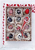 Red and black, hand-painted Easter eggs in a seedling tray lined with straw