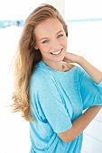 Portrait of beautiful blonde woman wearing turquoise top with hand in hair, smiling