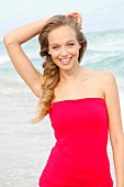 Portrait of beautiful blonde woman wearing red dress standing on beach, smiling