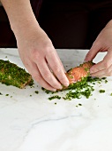 Close-up of hand covering salmon fillet with herbs