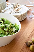 Bowl of lettuce salad and stack of plates with spoons