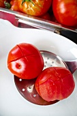 Close-up of two red tomatoes cut in cross on ladle with holes