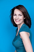 Portrait of pretty woman with brown hair wearing blue top, smiling, side view