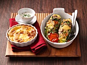 Stuffed zucchini in casserole and baked speckschmarren in ramekin on wooden board