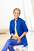 Cheerful woman with light blonde hair in blue shirt over yellow blouse and blue pants