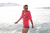 Frau im blauen Bikini, transparente Bluse in pink am Strand im Wasser