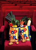 Various vegetables in popcorn bags and potatoes spilled on red cinema seat