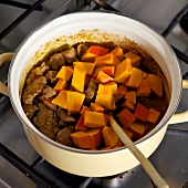 Close-up of pieces of pumpkin being added with mixture of meat in casserole, step 3