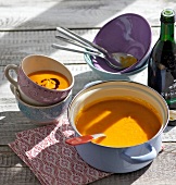 Cream of pumpkin soup in sauce pan and cups