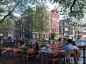 People at cafe on pavement with canal houses in background, Amsterdam, Netherlands