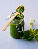 Glass jar of basil pesto with wooden spoon on top