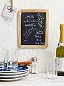 Notes on a blackboard, a stack of crockery and a bottle of sparkling wine a student kitchen