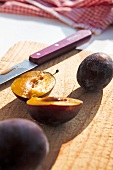 Halved plums with knife on chopping board