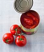 Three whole tomatoes besides tomato sauce in tin