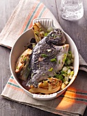 Baked sparidae with artichokes and fennel leaves in serving bowl
