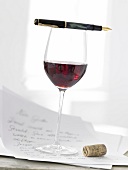 Glass of red wine with pen, letter and cork