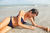 Brünette Frau in blauem Bikini liegt lachend im Meer
