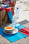 Close up of napkin spread with halved melon and cutlery on it and picnic basket on side