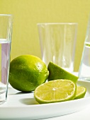Close-up of whole, halved and sliced limes with glasses on table