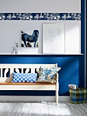 Basket of magazines next to rustic, white wooden bench against blue and white wall with frieze