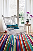White wicker chair with cushion on colourful striped carpet