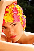 A woman wearing makeup with a colorful bathing cap looking into the camera