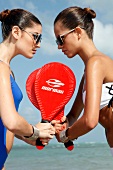 Two women wearing Sunglasses, holding beach bat, standing face to face