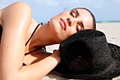 Woman in a black bikini lies relaxed in the sand on the beach