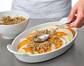 Sauteed bread crumbs and parmesan being spread on vegetable slices in baking dish