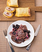 Beef with prunes on plate and pork on wooden board 