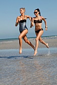 Two women in swimsuits and bikinis running on the beach