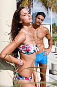 Mann in blauer Badehose taxiert Frau im Bikini